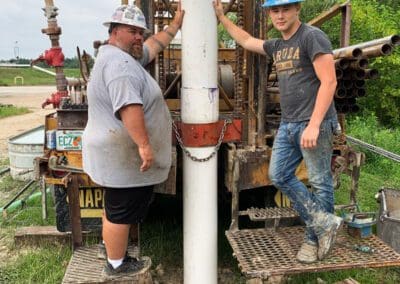 2 Bronco Boys standing by a well drilling rig