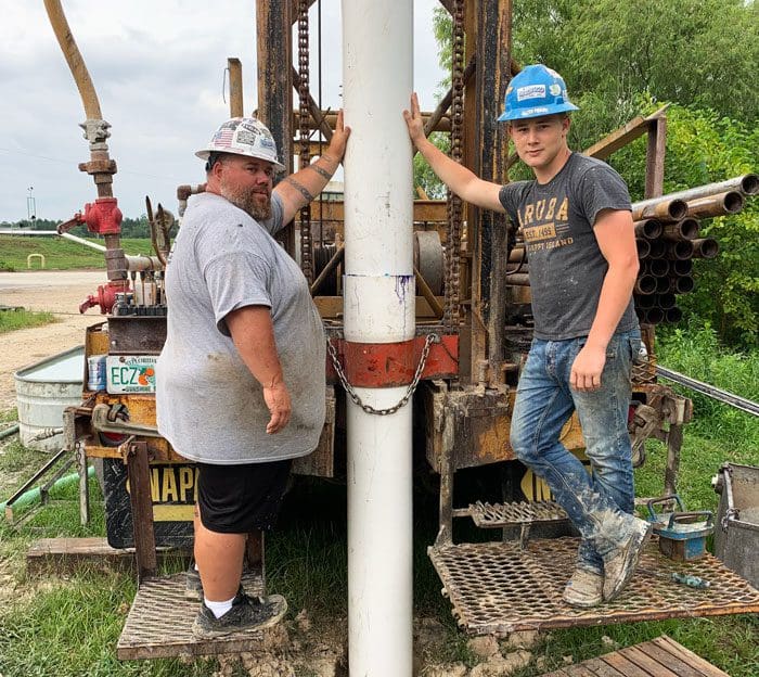 2 Bronco Boys standing by a well drilling rig